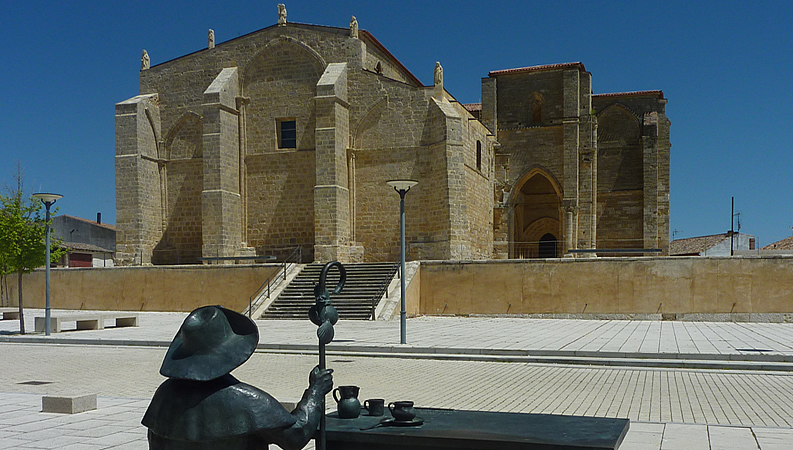 Estatua del mesonero Pablo Payo con la iglesia de Santa María la Blanca al fondo en Villalcázar de Sirga